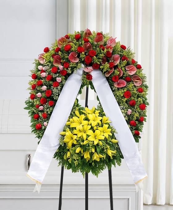 Corona funebre con fiori di stagione dai colori caldi, su cavalletto, per una cerimonia a Bologna