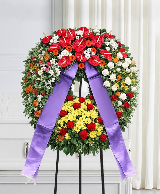 Corona funebre con fiori dai toni caldi con nastro, composizione per un funerale a Bologna