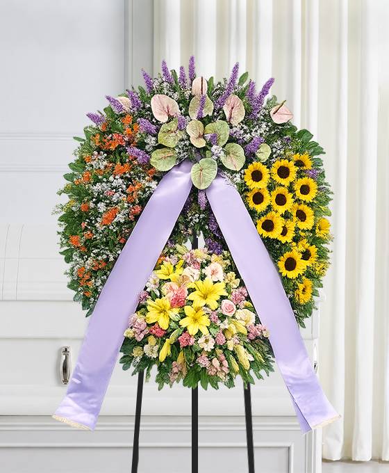 Corona funebre a settori con girasoli, gerbere e anthurium montata sul cavalletto