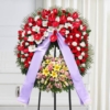 Corona funebre in rosso e bianco con fiori colorati montata su cavalletto, omaggio floreale a Bologna