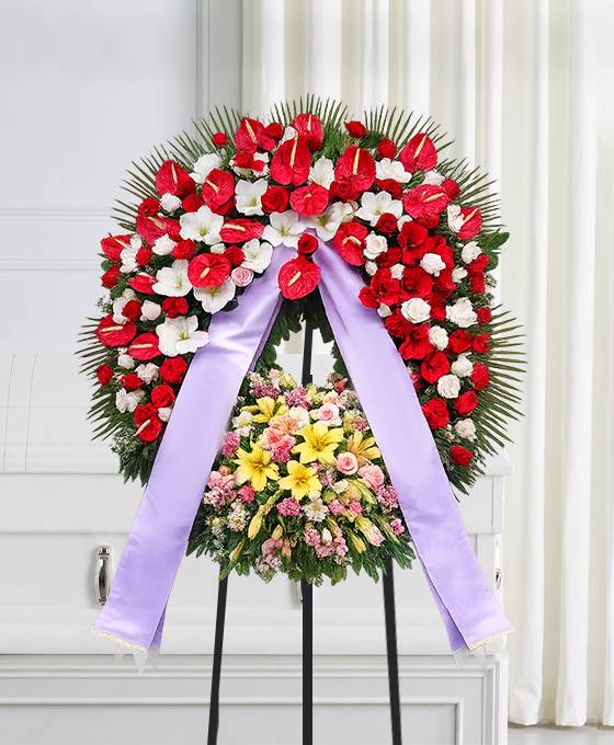 Corona funebre in rosso e bianco con fiori colorati montata su cavalletto, omaggio floreale a Bologna